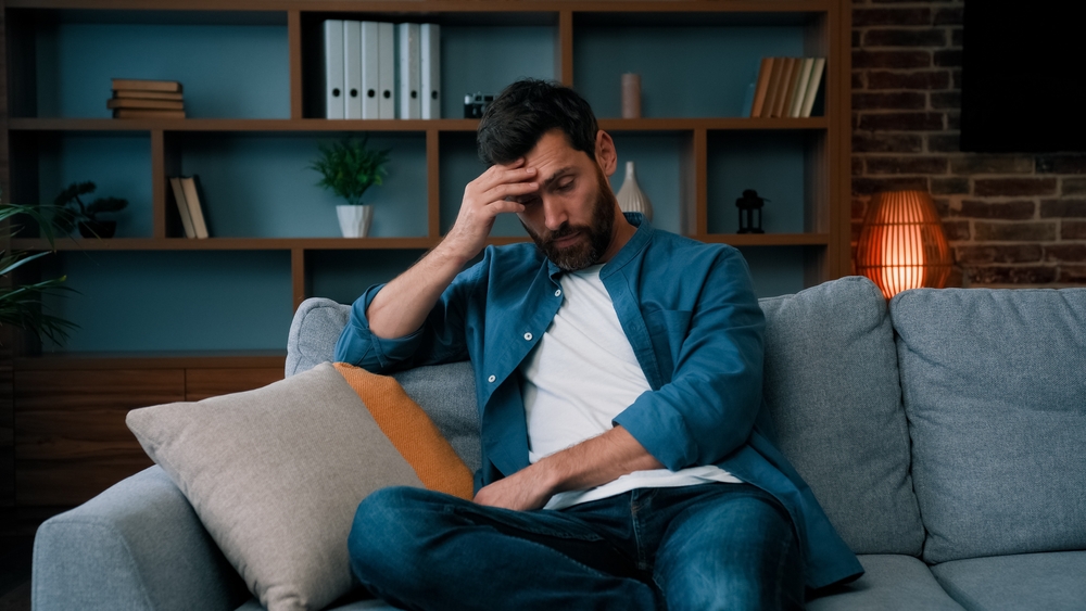 Tired upset father caucasian bearded man sit on sofa frustrated about hard working day at home stressed worried single guy lonely male irritated anxious feel unwell exhaistion lack of energy stress